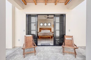 Une chambre à coucher comprenant un lit, deux fauteuils en osier et une porte-fenêtre coulissante donnant sur la pièce.