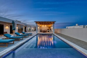 Ein Pool mit Liegestühlen, einer überdachten Sitzgelegenheit und Blick auf den Himmel.