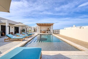 Ein Poolbereich mit Liegestühlen, einer Pergola und Blick aufs Meer.