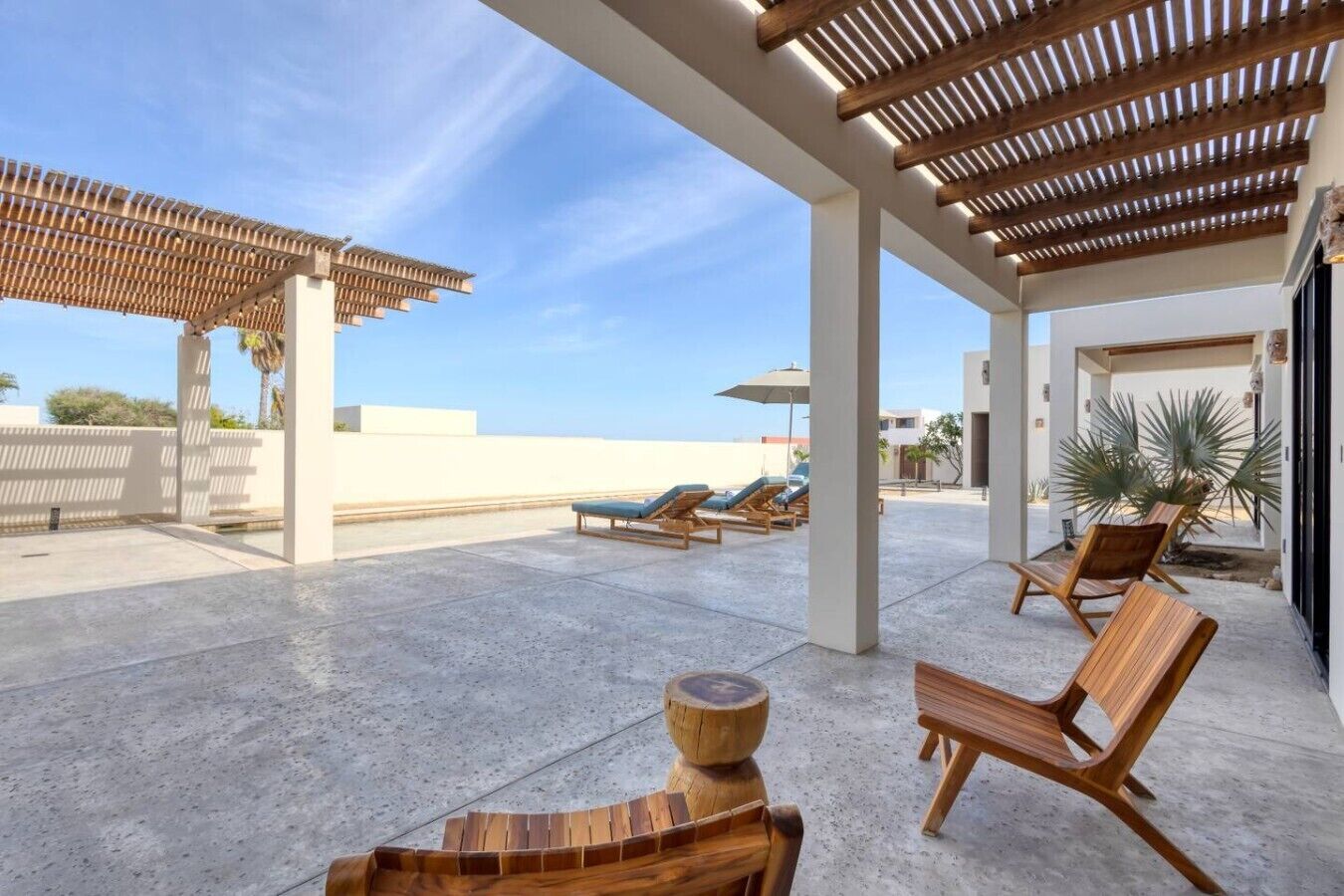 A covered outdoor area with lounge chairs, a wooden table, and a pergola.