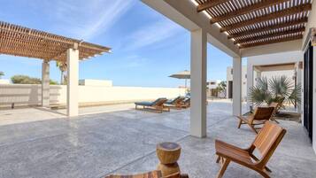 A covered outdoor area with lounge chairs, a wooden table, and a pergola.