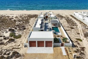 Un hôtel situé en bord de mer, composé de plusieurs bâtiments blancs, doté d’une piscine et bordé d’une plage de sable.