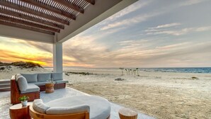 A beachside lounge with a sofa, chairs, and a wooden table, overlooking the ocean. - Oceanfront Luxury in East Cape Private Beachfront (Ligth House Point States)