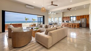 A spacious living area with a large sofa, a dining table, and a kitchen with wooden cabinets and a stainless steel refrigerator. - Oceanfront Luxury in East Cape Private Beachfront (Ligth House Point States)