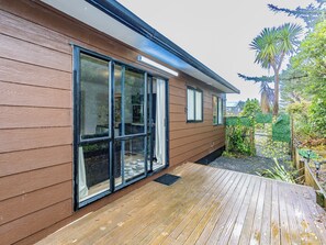 Ein modernes Haus mit großen Schiebegläsern, einer Holzterrasse und einem Garten mit verschiedenen Pflanzen.