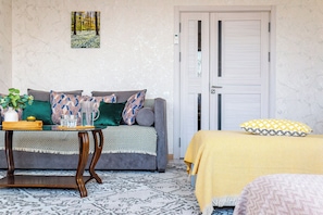 Una habitación con un sofá, una mesa con una bandeja, una cama con una manta amarilla y una puerta.