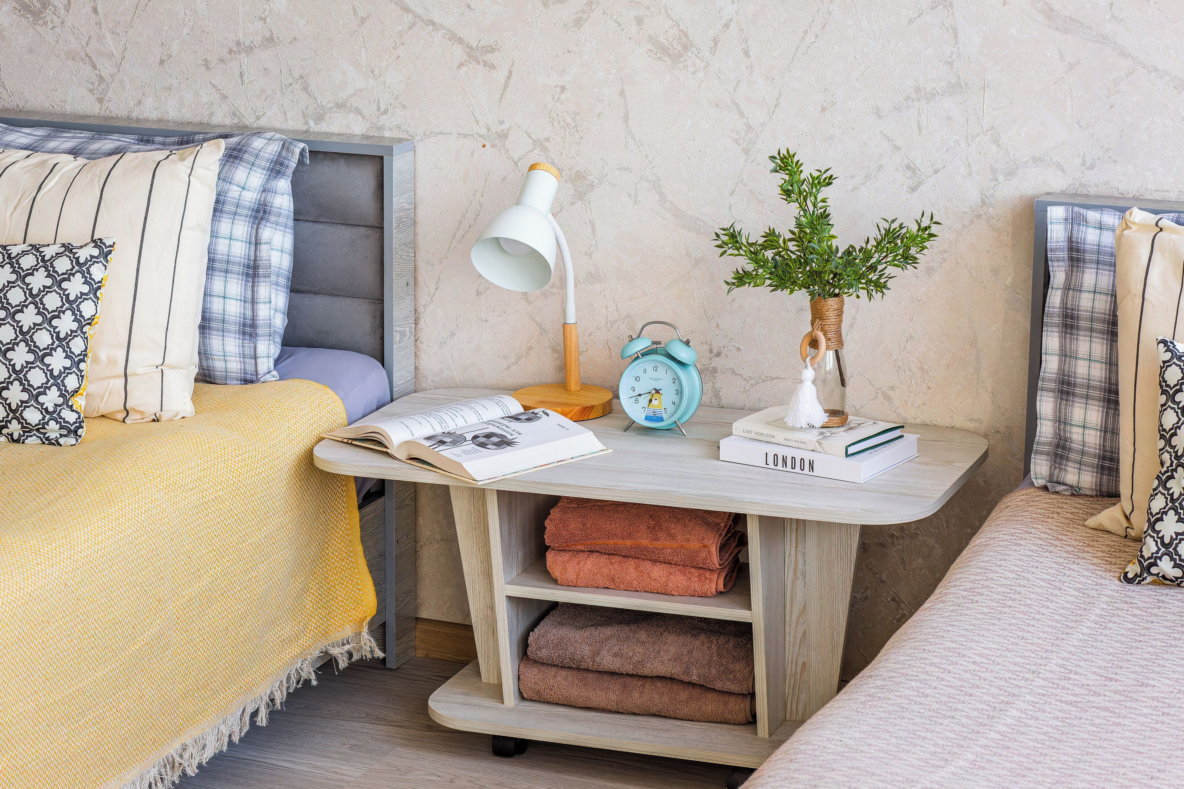 Une chambre à coucher avec un lit, une table de chevet, une lampe, une horloge et une petite plante.