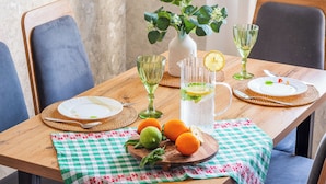 Ein Holztisch mit karierter Tischdecke, eine Wasserkanne mit Zitronenscheibe und eine Vase mit Grünpflanzen.