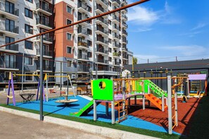 A playground with various play structures, surrounded by a building with multiple balconies and air conditioning units. - Chaqar 235 (Tashkent)