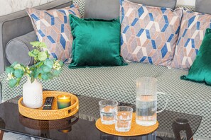 A bed with patterned bedding, a green pillow, a remote control, a candle, and glasses on a table. - Chaqar 235 (Tashkent)