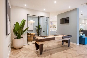 A modern indoor pool table with a wooden finish, a potted plant, and a dining area in the background. - 2BR Modern Apartment | 12 Mins to Heathrow (Staines-upon-Thames)