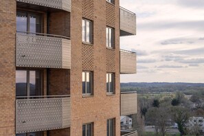 A multi-story building with perforated balconies, large windows, and a view of a rural landscape. - 2BR Modern Apartment | 12 Mins to Heathrow (Staines-upon-Thames)