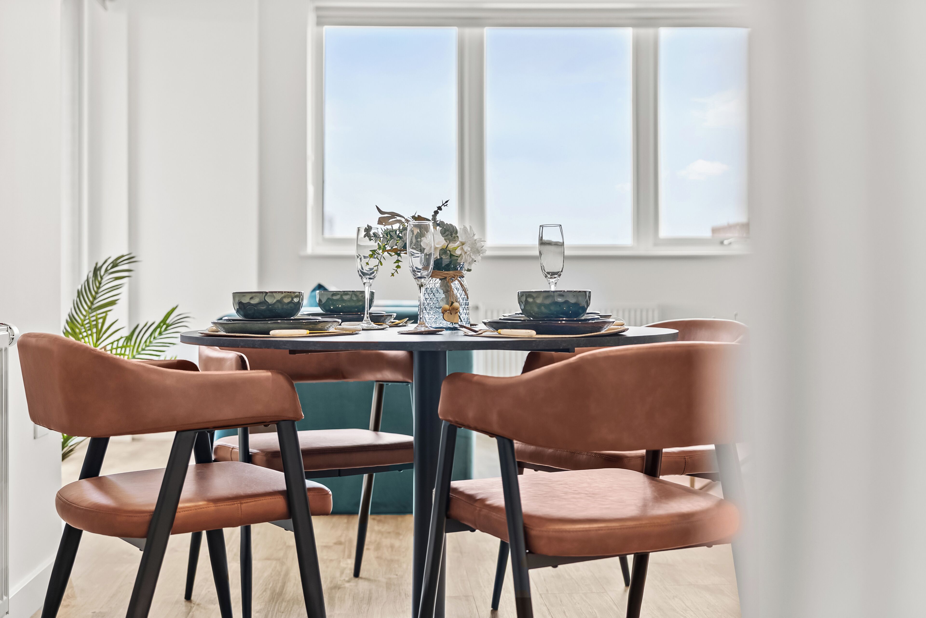 A dining table with chairs, a vase with flowers, and a window with a view.