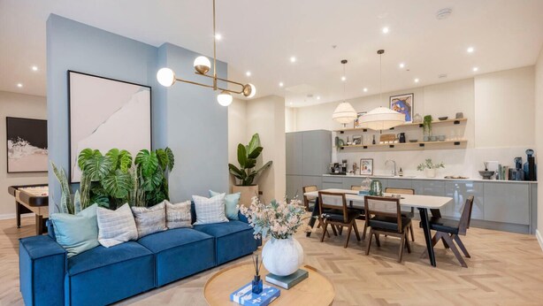 Ein modernes Wohnzimmer mit einem blauen Sofa, einem Essbereich mit Holztisch und einer Küche mit Bar.