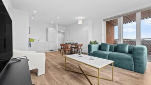 Ein modernes Wohnzimmer mit Fernseher, einer Couch, einem Essbereich und einem Balkon mit Aussicht.