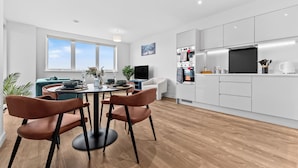 Eine moderne Küche mit weißen Schränken, ein Essbereich mit einem runden Tisch und Stühlen sowie ein großes Fenster.