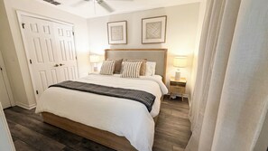 Un dormitorio con una cama, lámparas de noche, una puerta y dos cuadros en la pared.
