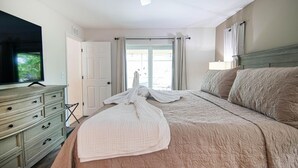 Una habitación de hotel con cama, televisión, cómoda y ventana con cortinas.