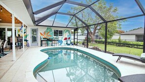 Una piscina interior con techo de cristal, un mural en la pared y una zona de patio con sillas.