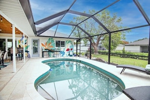 Une piscine intérieure dotée d’un toit en verre, d’une fresque murale et d’un espace patio avec des chaises.