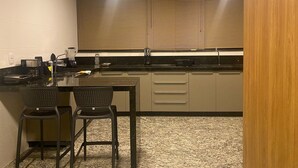 A compact kitchen with a central island, two bar stools, a coffee maker, and a built-in oven. - LK Lourdes 11 (Belo Horizonte)
