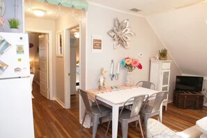 Un coin repas avec une table blanche, des chaises grises, un vase de fleurs et un élément décoratif mural.