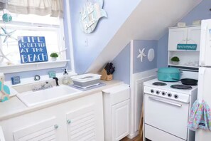 Une cuisine avec un four blanc, des placards blancs et une fenêtre sur laquelle est accrochée une pancarte indiquant : « La vie est plus belle à la plage. »