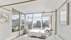 Ein modernes Schlafzimmer mit einem großen Fenster, einem Himmelbett und Blick auf die Stadt.