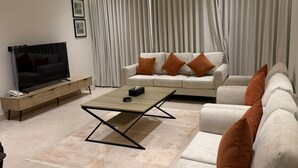 Uma sala de estar moderna com sofá, mesa de centro, TV e uma janela grande com cortinas.