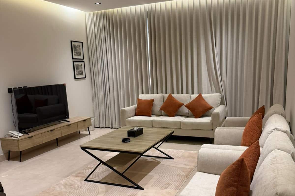Una sala de estar moderna con sofá, mesa de centro, televisor y un ventanal con cortinas.