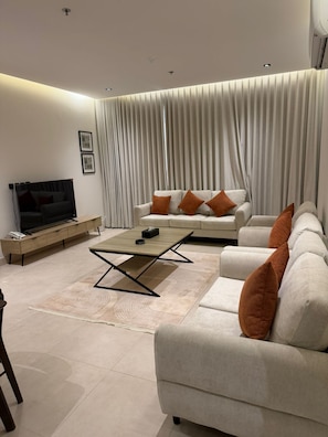 A modern living room with a sofa, a coffee table, a TV, and a large window with curtains.