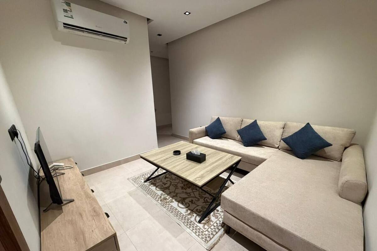 Una sala de estar moderna con un sofá, una mesa de centro, un televisor sobre un mueble bajo y un equipo de aire acondicionado.