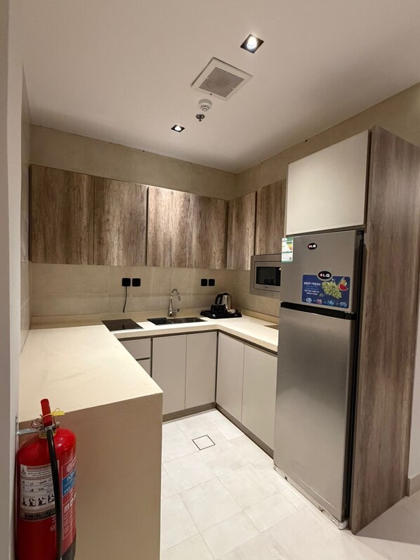A modern kitchen with wooden cabinets, a stainless steel refrigerator, a microwave, and a sink.