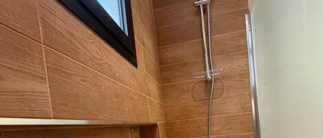 A modern bathroom with wooden paneling, a shower with a handheld showerhead, and a window above the sink.