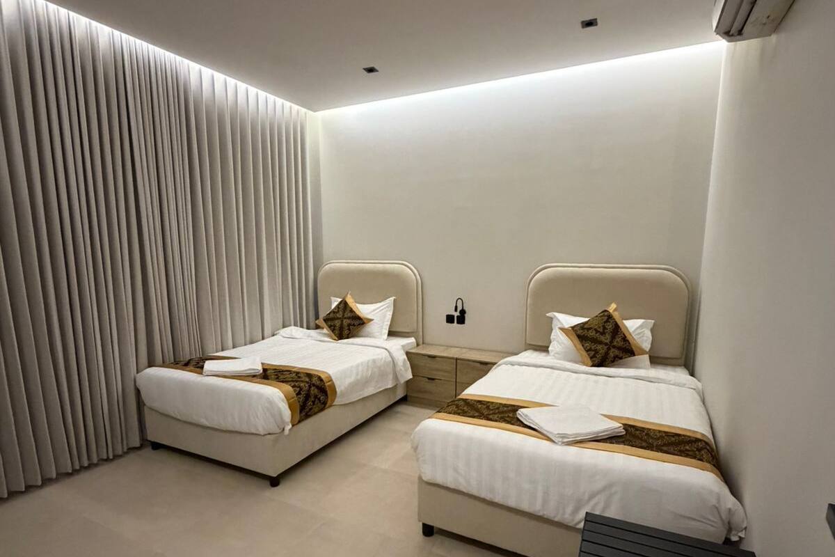 Una habitación de hotel moderna con dos camas, una mesita pequeña y un aire acondicionado instalado en la pared.