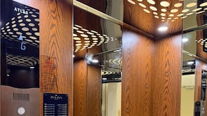 Interior de elevador com painéis de madeira, um visor digital e uma placa da AYA INN.