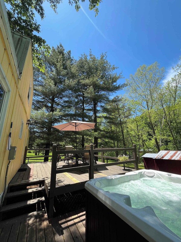 A wooden deck with a hot tub, a covered outdoor seating area, and a view of a forested area.