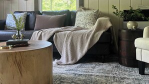 A cozy living room with a dark-colored sofa, a round wooden coffee table, and a patterned rug. - Charming Creekside Cottage with Hot tub (Laurelville)