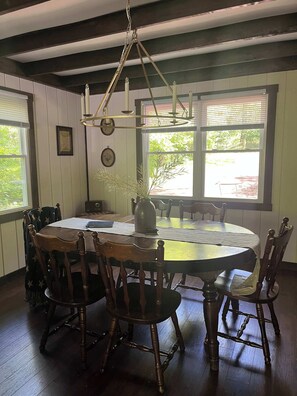A dining room with a round table, wooden chairs, a chandelier, and windows with blinds.