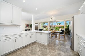A modern kitchen with white cabinetry, a large island, and a dining area with a view of the outdoors. - Premier 3-Bedroom Condo in Coveted Indian Wells Country Club, Discounted Rates! (Indian Wells)