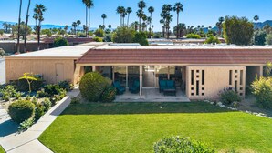 A modern building with a flat roof, a covered patio with outdoor furniture, and a well-maintained lawn. - Premier 3-Bedroom Condo in Coveted Indian Wells Country Club, Discounted Rates! (Indian Wells)