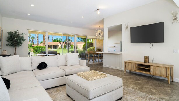 A modern living room with a sectional sofa, a flat-screen TV, and a dining area with a view of the outdoors. - Premier 3-Bedroom Condo in Coveted Indian Wells Country Club, Discounted Rates! (Indian Wells)