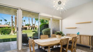 A dining area with a wooden table and chairs, a potted plant, and a view of a garden through glass doors. - Premier 3-Bedroom Condo in Coveted Indian Wells Country Club, Discounted Rates! (Indian Wells)