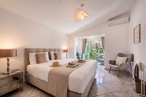 A bedroom with a large bed, bedside tables, a lamp, a hat on the bed, and a chair. - The Beach House - Villa walking to the beach (Albufeira)