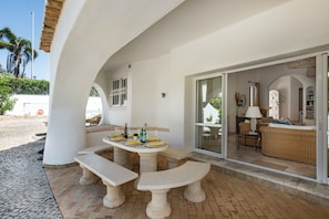 An outdoor patio with a table set for dining, a wicker sofa, and a sliding glass door leading to an interior space. - The Beach House - Villa walking to the beach (Albufeira)