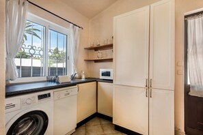 Une cuisine compacte équipée d’un lave-linge, d’un four à micro-ondes et d’une fenêtre avec des rideaux.