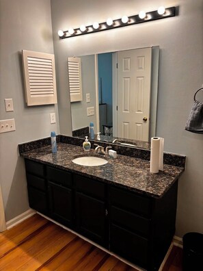 Une salle de bain avec un lavabo doté d’un plan de travail en granit, un grand miroir, des luminaires et un porte-serviettes.