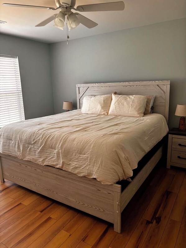 Une chambre à coucher avec un lit, une tête de lit en bois, des tables de chevet et un ventilateur de plafond.