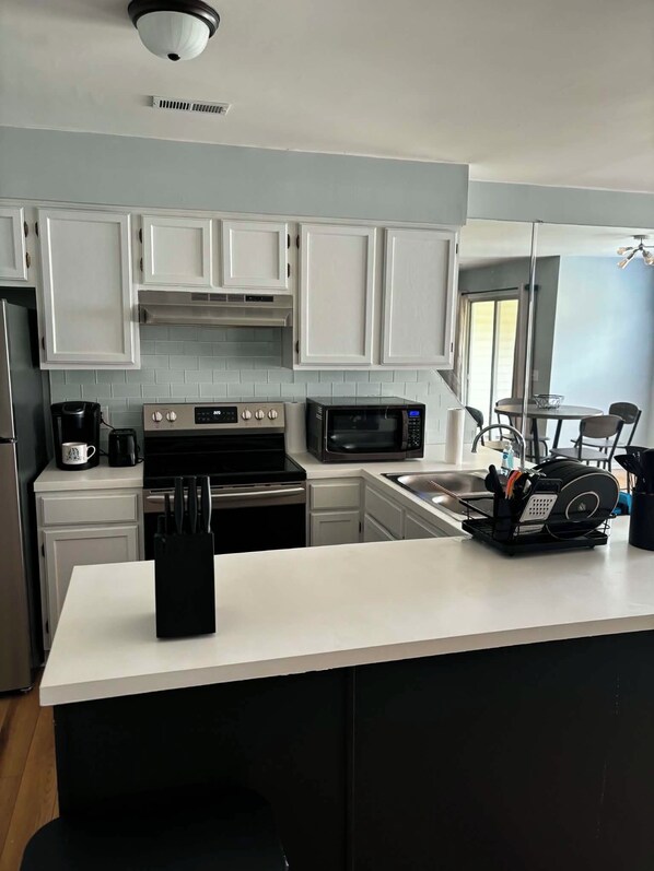 A modern kitchen with white cabinets, a microwave, a coffee maker, and a sink.
