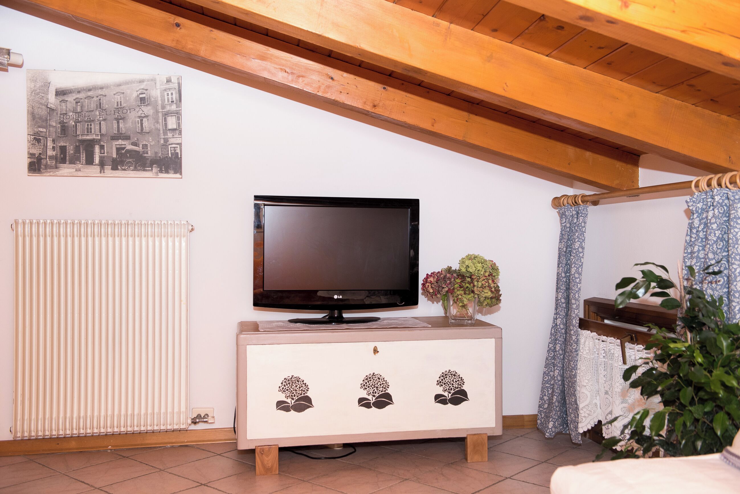 A living room with a television on a wooden cabinet, a radiator, a piano, and a wall-mounted picture.